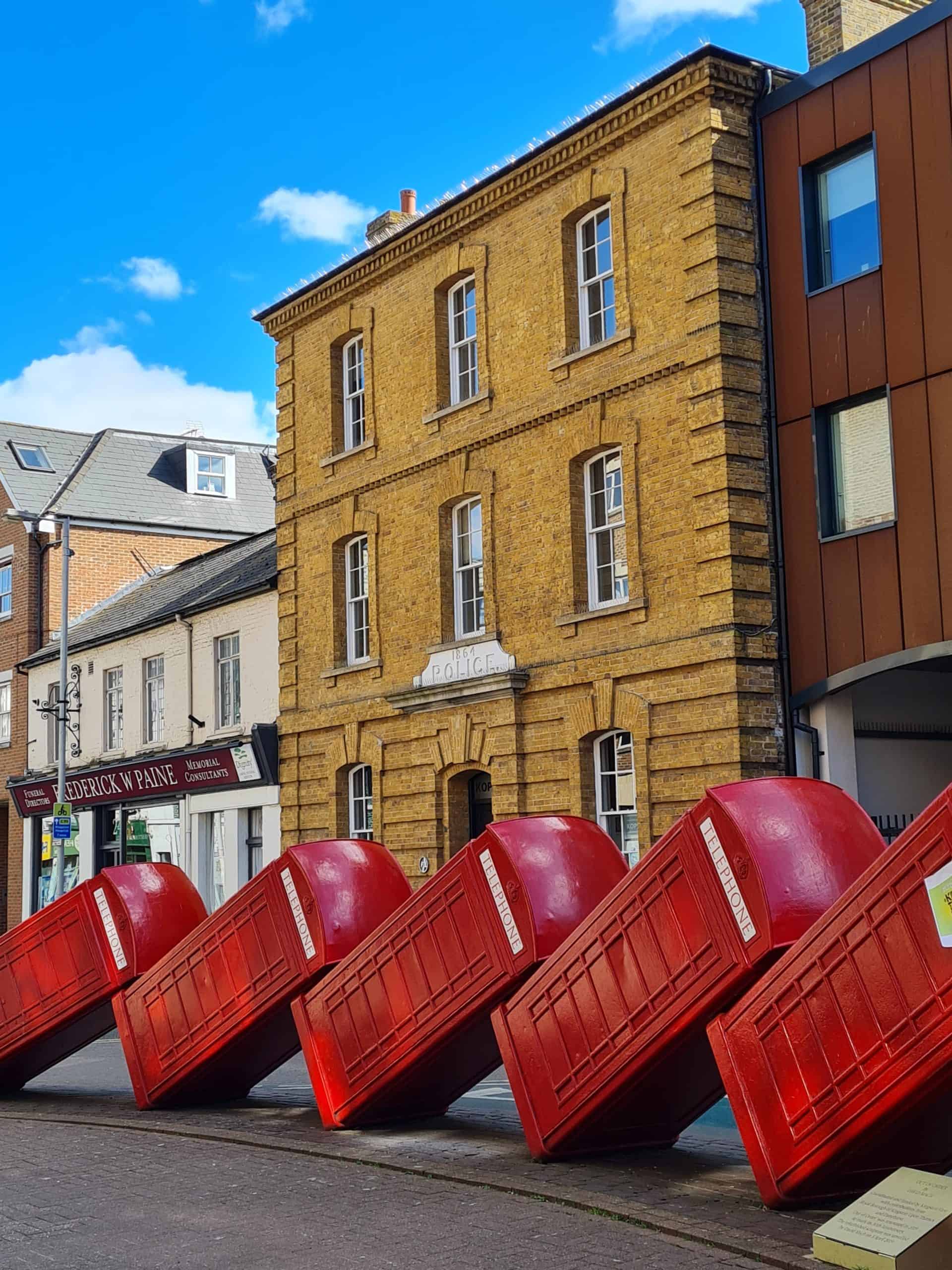 a photo of a artwork with red telephone boxes all leaning over on top of each other like a fallen stack of dominos.