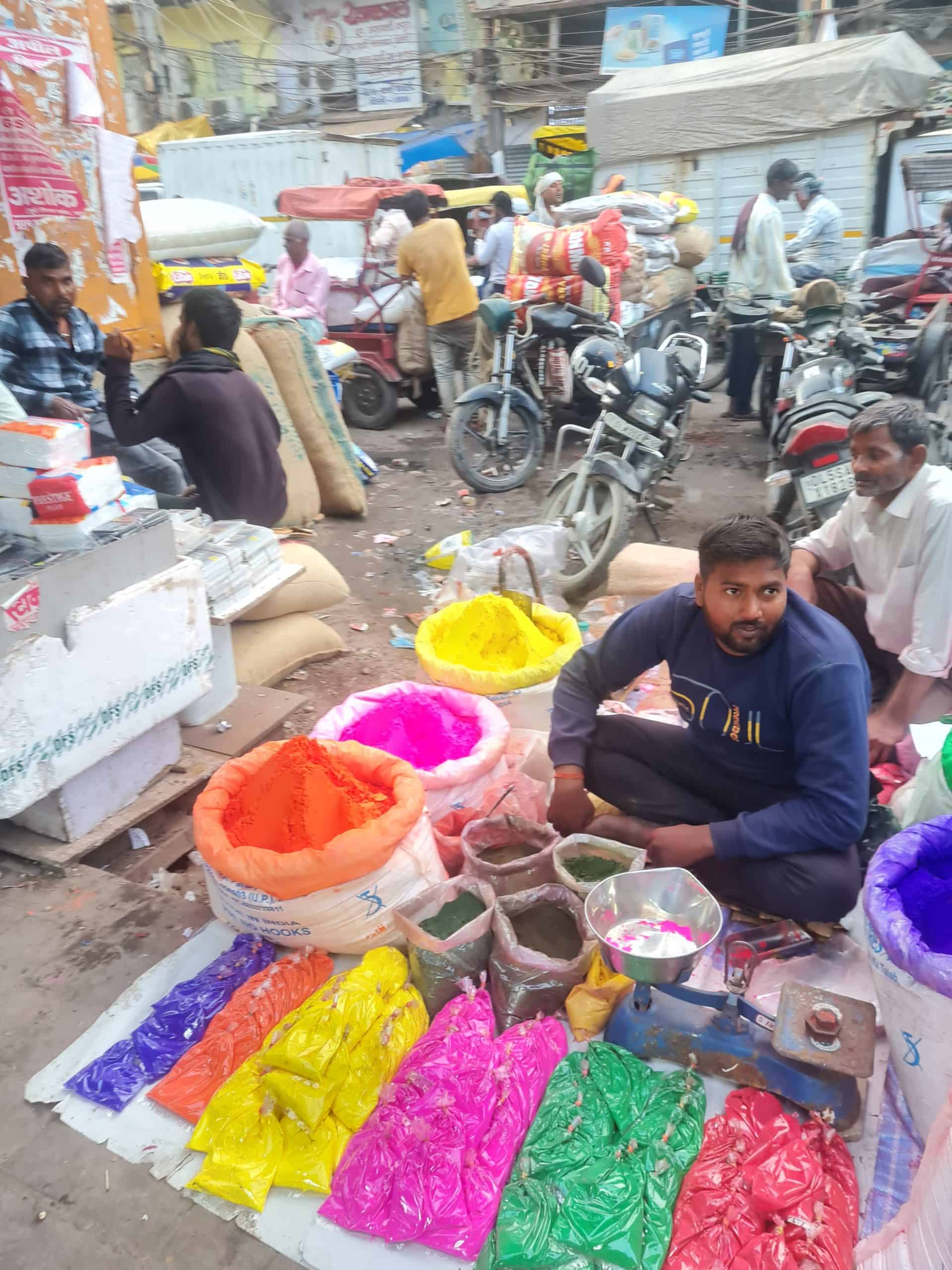 A man sitting on the ground with the colourful powders surrounding him in the market