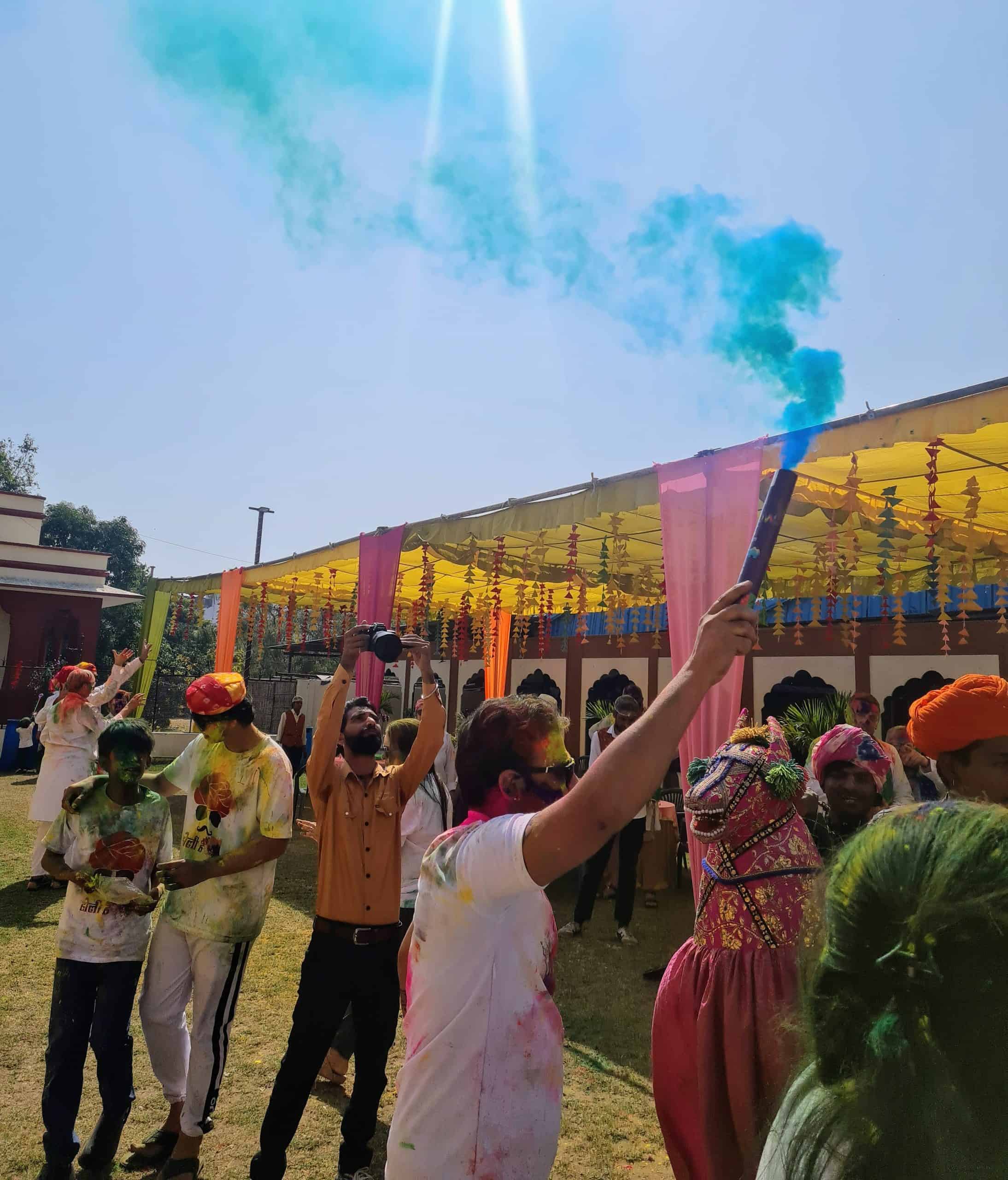 A indian man holding a cracker full of blue powder holding up to the sky with the blue powder coming out