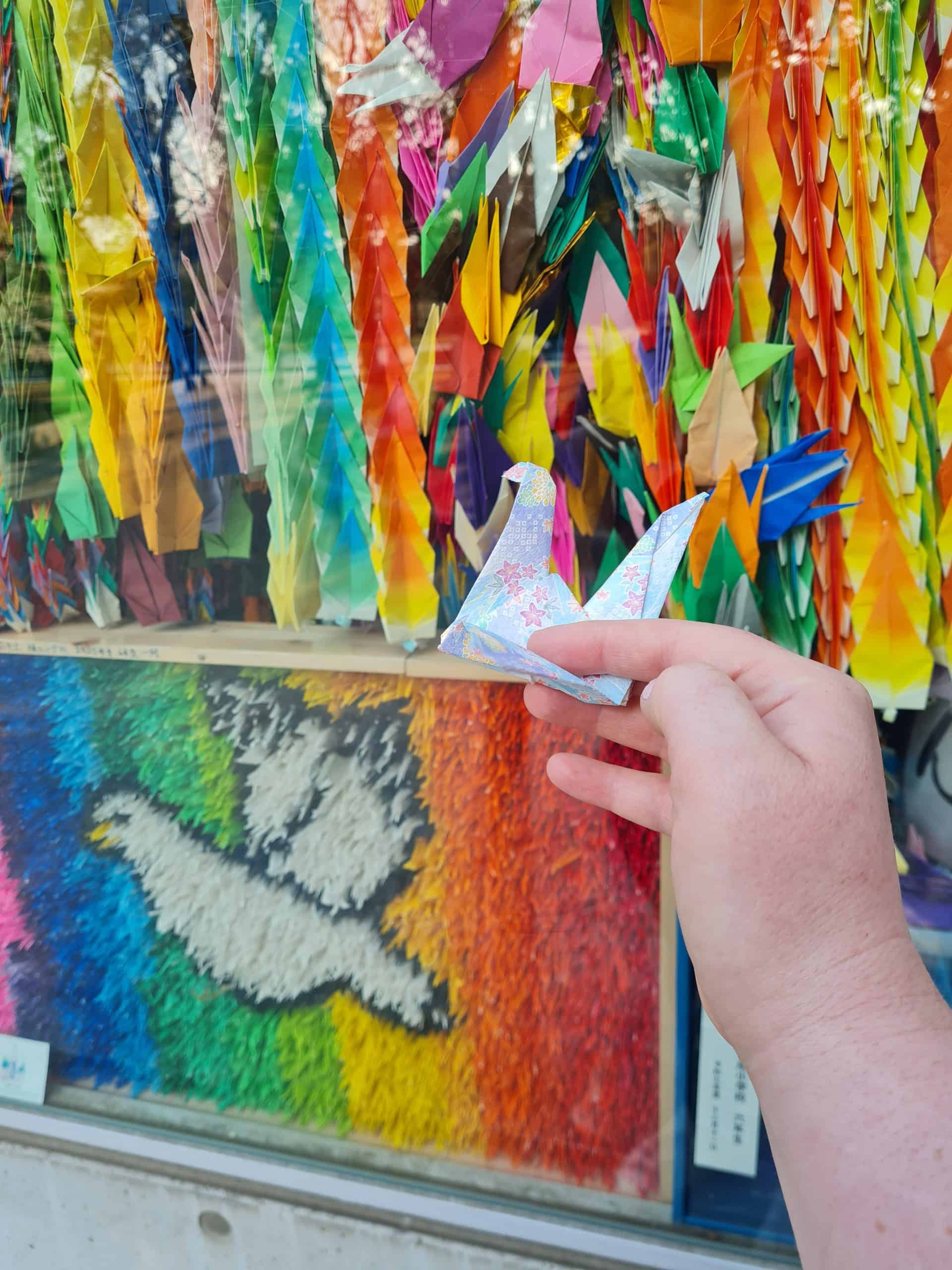 holding a paper crane with 1000's of paper cranes in the back ground at the childrens memorial in Hiroshima