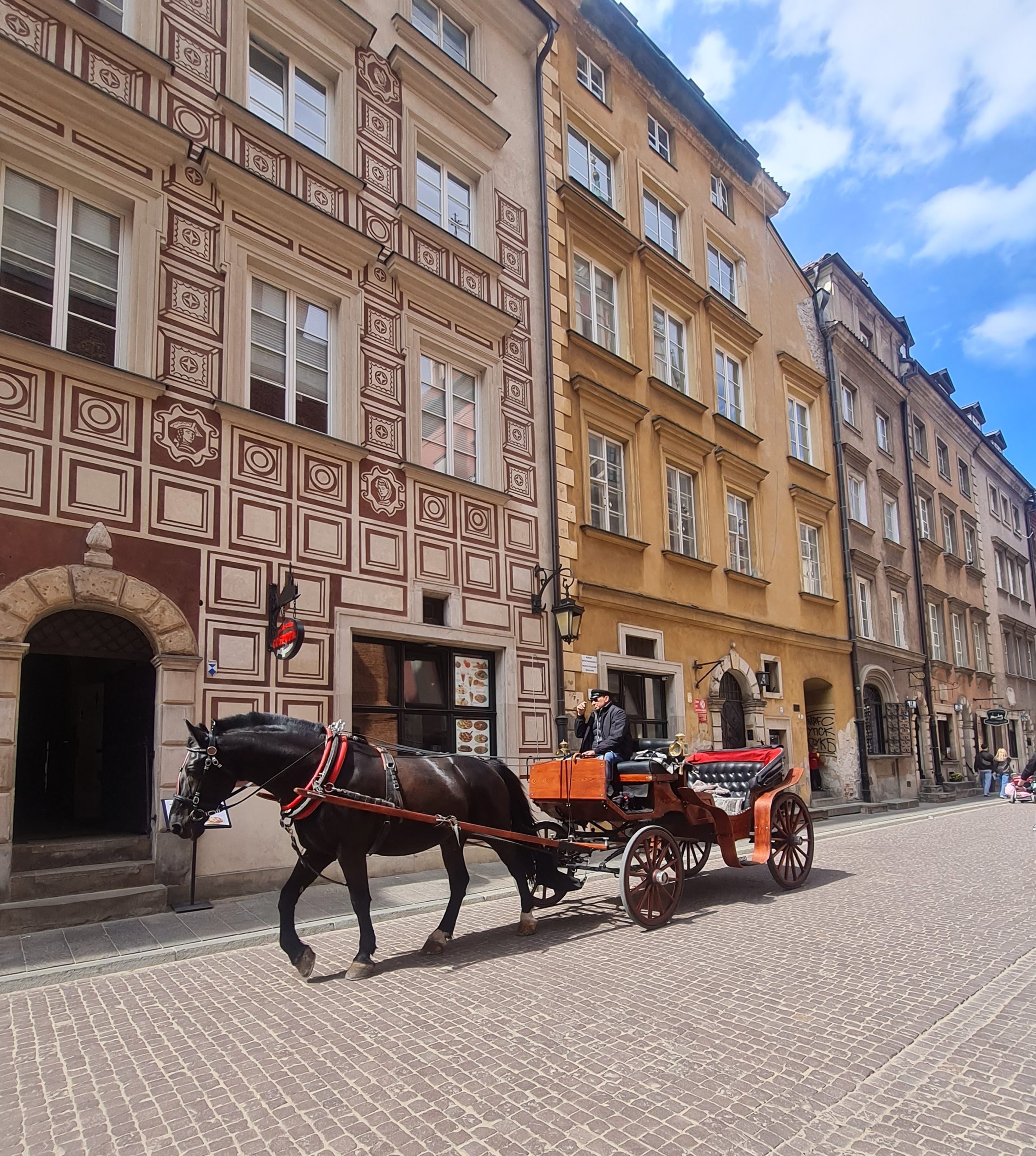 A man with a horse drawn carriage in the streets of the old town of warsaw with the historic buildings behind him