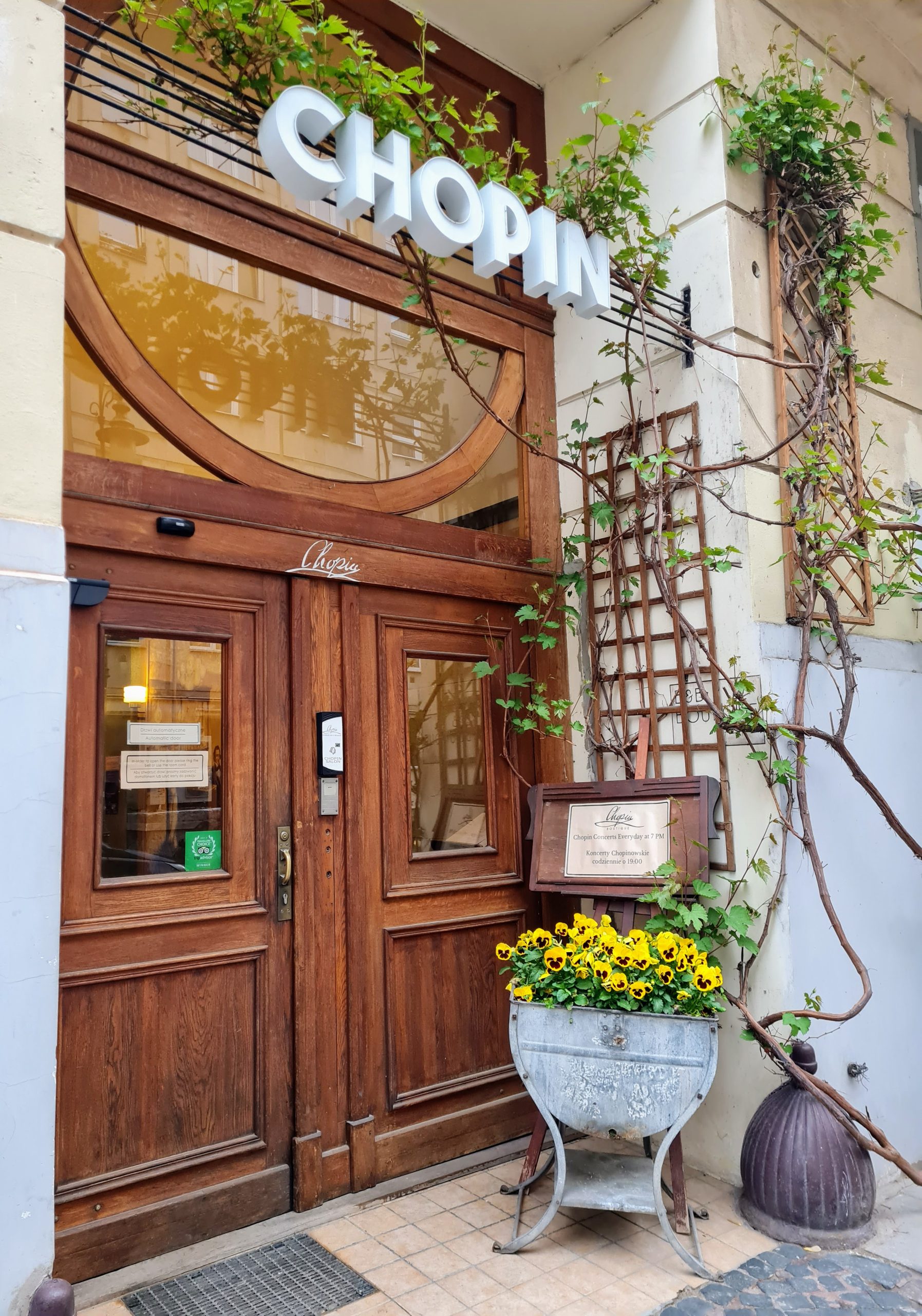 the front wooden doors of the Chopin Salon in Warsaw, with the sign chopin above and a pot of yellow flowers beside the door