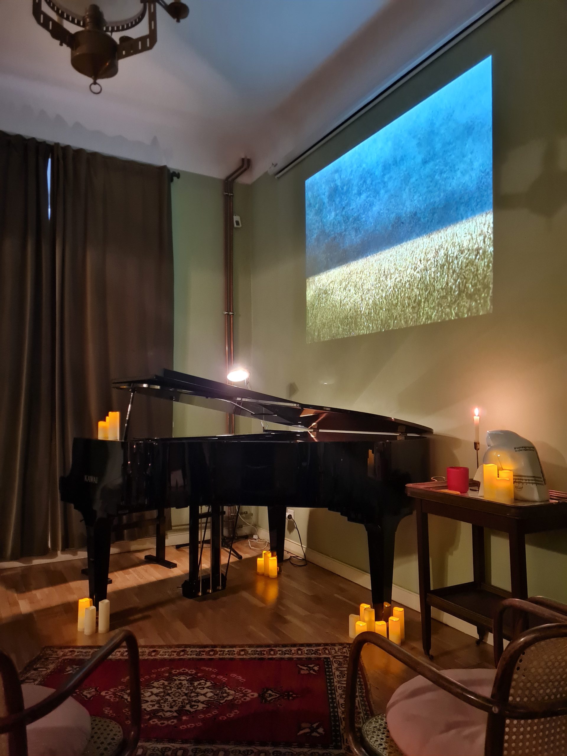 inside the Chopin salon with the piano and candles all around lit. On the wall next to the piano is a sideshow of landscape paintings